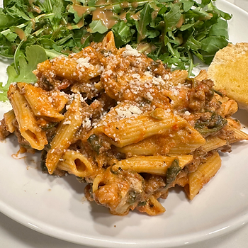 Pasta with red sauce and cheese on a white plate, accompanied by a green salad with dressing and a bread roll.