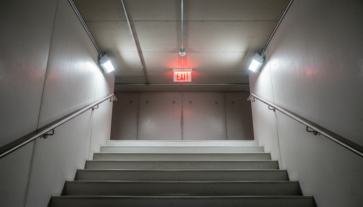 Low-angle view of emergency lighting and exit signage above a clean stairwell