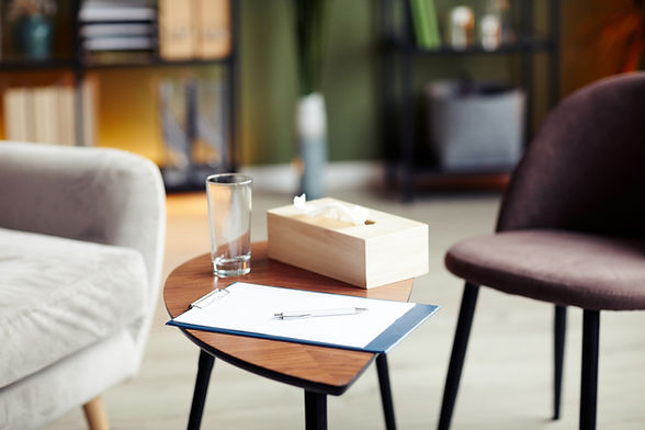 Clipboard with blank sheet, glass of water and napkin box on table in office of therapist.