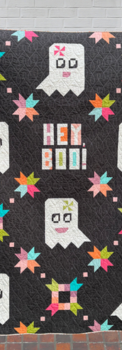 Dark quilt with smiling ghosts and colorful stars, reading "HEY BOO!"