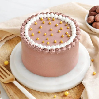 A pink colour cake with golden pearls on top of ot