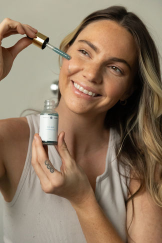 Young woman holding a beauty product by Honestly Essential while smiling.