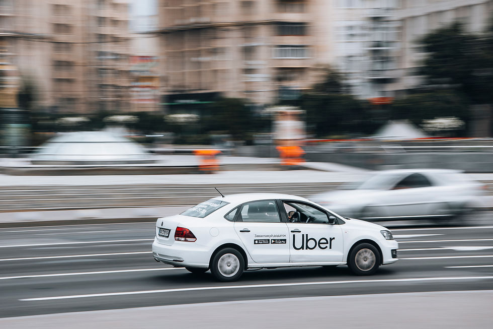 Uber car in motion on a city street, blurred background with buildings and a second car. Urban setting with a dynamic feel.