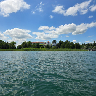 Blick vom Kajak auf die Schlosswirtschaft Herrenchiemsee am Ufer der Herreninsel während einer Kajaktour auf dem Chiemsee.