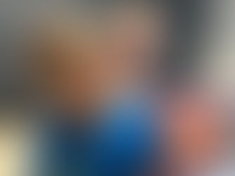 Smiling boy in a blue shirt and a woman behind him hold a "Cariboo" game box. They're in a room with a chalkboard background.