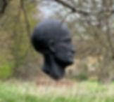 A sculpture of a giant head in amongst grasses and trees