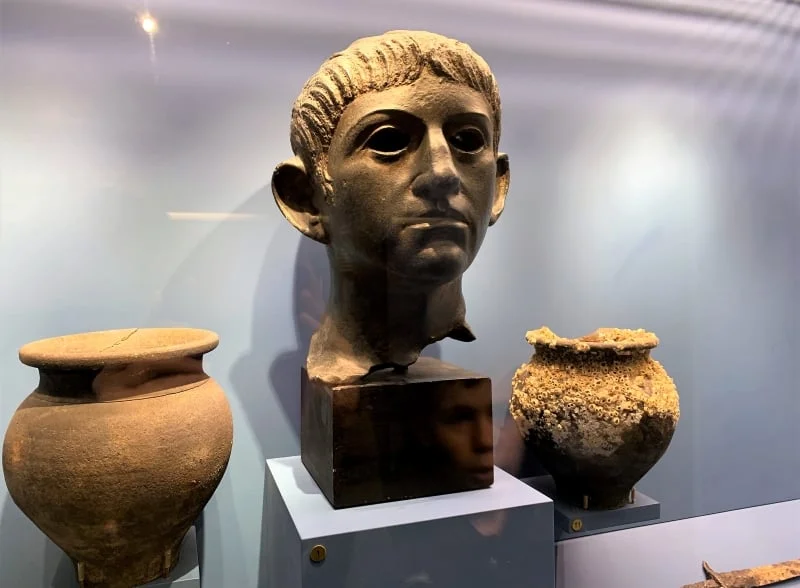 A Roman statue head with two Roman pots in a display case in Aldeburgh Museum