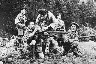 An old black and white photo of young men wearing berets with guns in a wood.