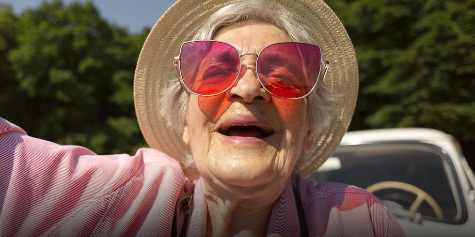 An elderly woman wearing a wide brimmed hat and large pink sunglasses laughing in a car, used as the hero image for the Mullis and Peake Solicitors brand refresh and design partnership case study by Julie Nicholls