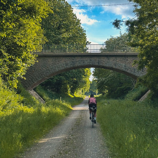 cyclist on a gravel path, crossing under am arched bridge