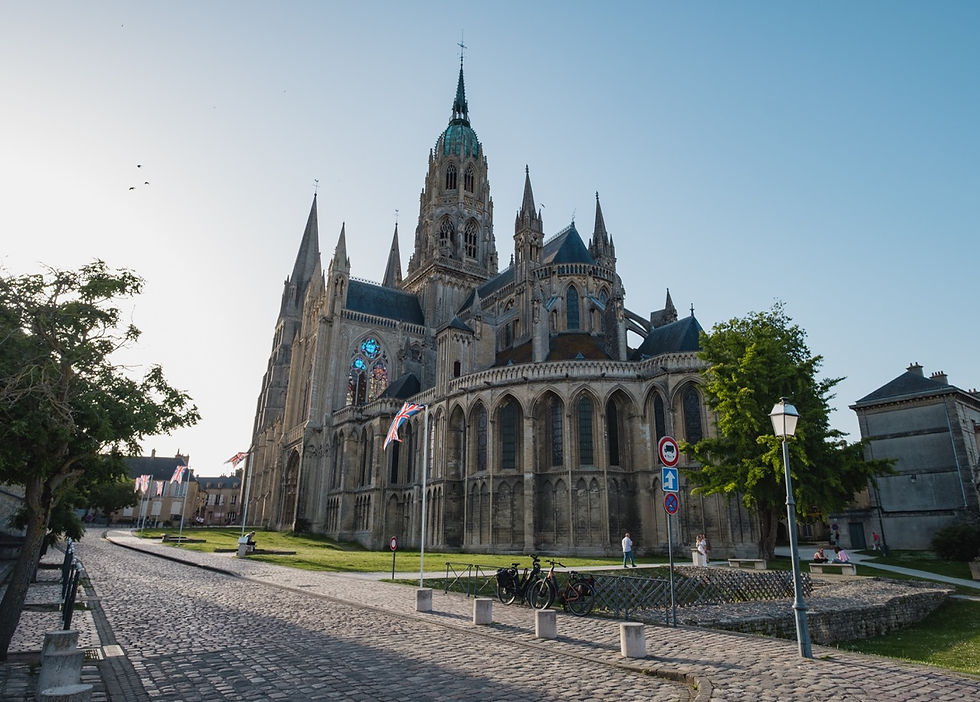 Grand Gothic cathedral beside a cobblestone street, with Union Jack flags, bicycles, a few people, and a clear blue sky