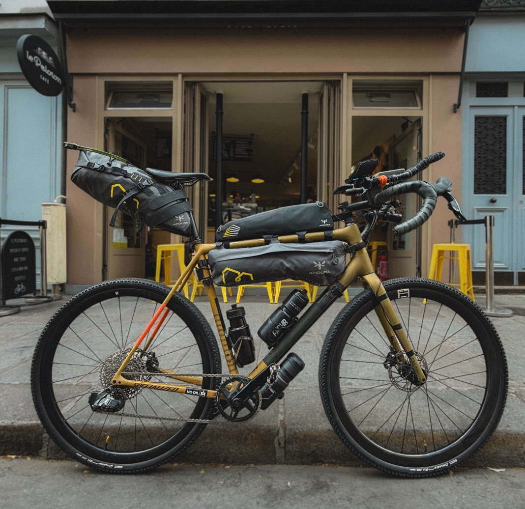 Loaded gravel bike parked outside a cafe with yellow stools