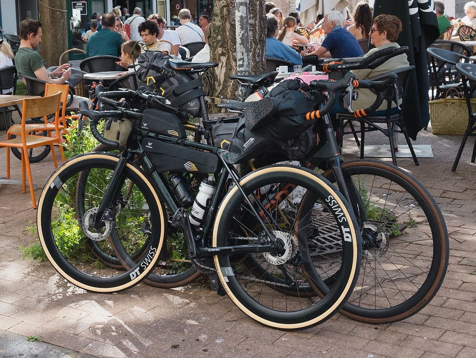 Two loaded touring bikes parked outside a busy café, with patrons seated at tables and DT SWISS visible on the wheels.