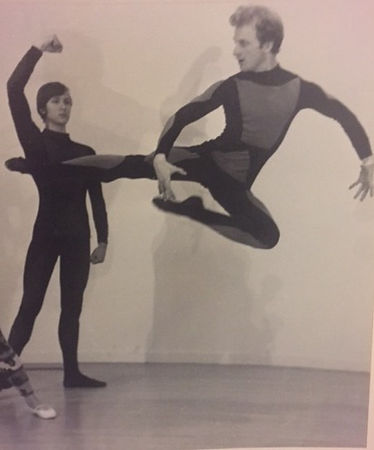 two men in unitards, one is leaping and the other is raising his fist