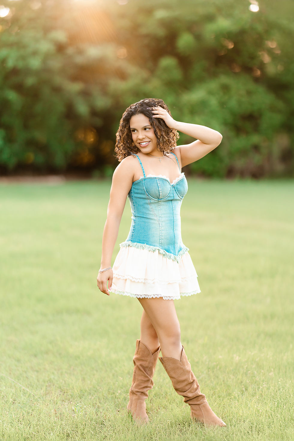 Senior standing in field taking senior portraits at sunset.
