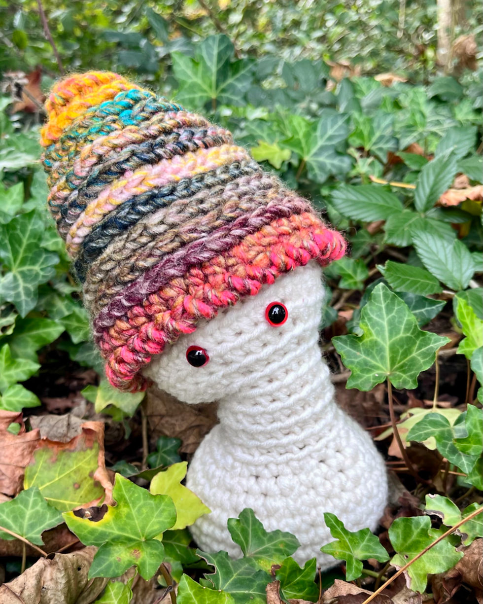 Morel the Mushroom Wisp, a handmade crochet woodland character, sitting among green ivy in his colourful cap