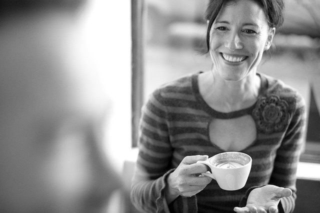 a woman smiling, holding a latte in a white coffee cup
