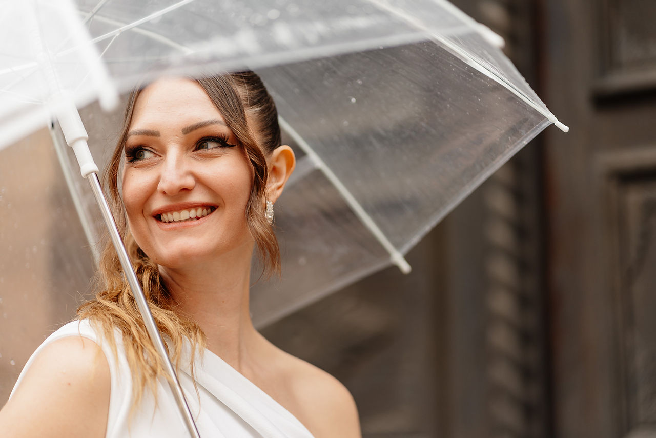 Braut lächelt unter transparentem Regenschirm bei Regen am Hochzeitstag
