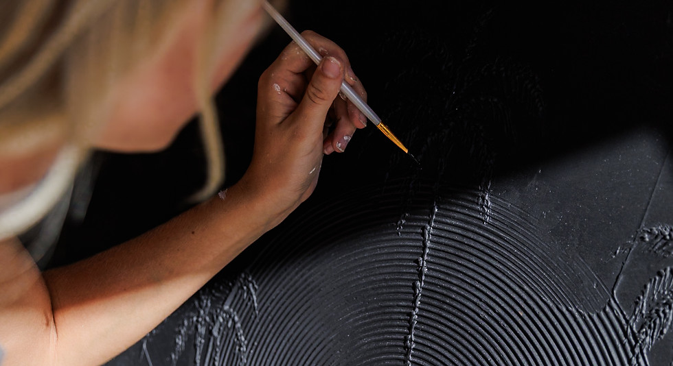 Emma painting fine detail on a black textured custom art piece