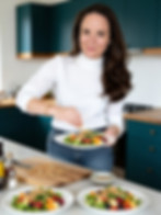 Aline Paqualetto, nutricionista e naturopata brasileira-britânica, polvilhando nozes sobre uma salada fresca na cozinha.