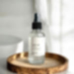 salty air room spray sitting on a wooden tray on a vanity in a bathroom with a white bathtub in the background.