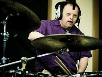 Michael White, Drummer of Heavy Load is a white man appearing to have Downs syndrome with wearing headphones and playing the drummers