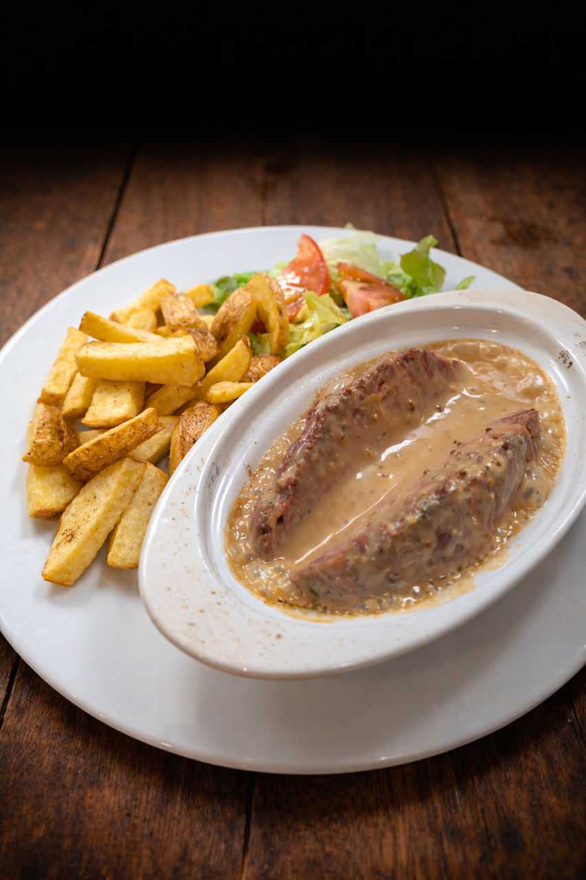Pièce de viande nappée de sauce crémeuse accompagnée de frites et salade