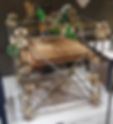 A 3D printer with a metal frame and green components on display in a museum. Wooden base, neutral background, label partially visible. The first RepRap machine at the Science Museum in London.