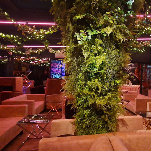 sur l'image on peut observer une colonne végétale tres fournis de feuillage artificiel dans un espace de vie aec des canapés