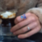 En hand med en blå och lila ring och en pärlring håller en kopp med Irish Coffee