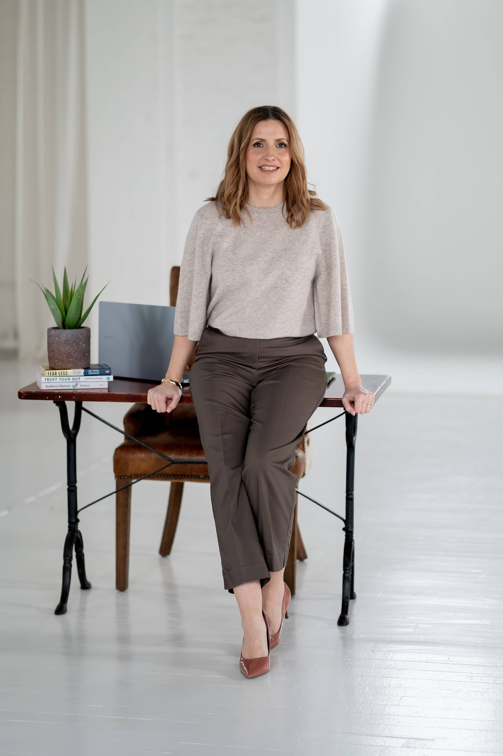 Full length portrait of the coach standing beside a desk in a bright Liverpool studio, showcasing understated authority.