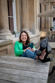 A woman in a green blazer sits outdoors with her feet up on a wooden table, smiling and holding a smartphone, captured by Liverpool brand photography.