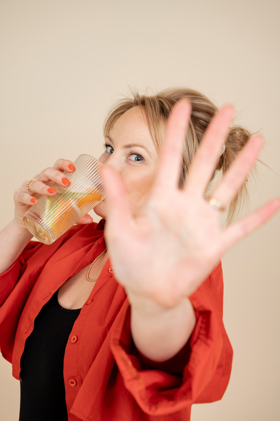 Web designer playfully holds up her hand while sipping juice from a glass.