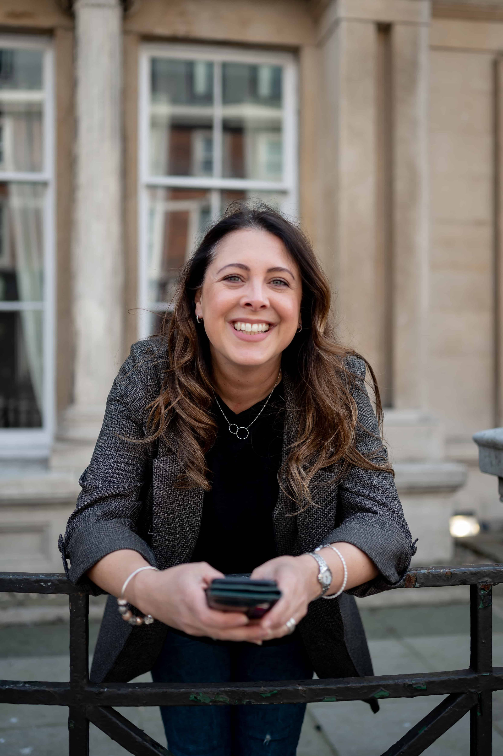 A smiling woman leaning on a railing in front of a building during a brand photoshoot.