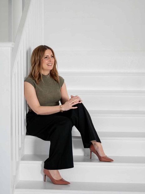 Woman sitting on white stairs during a brand photoshoot, elongated seated pose with legs crossed, editorial personal brand photography.