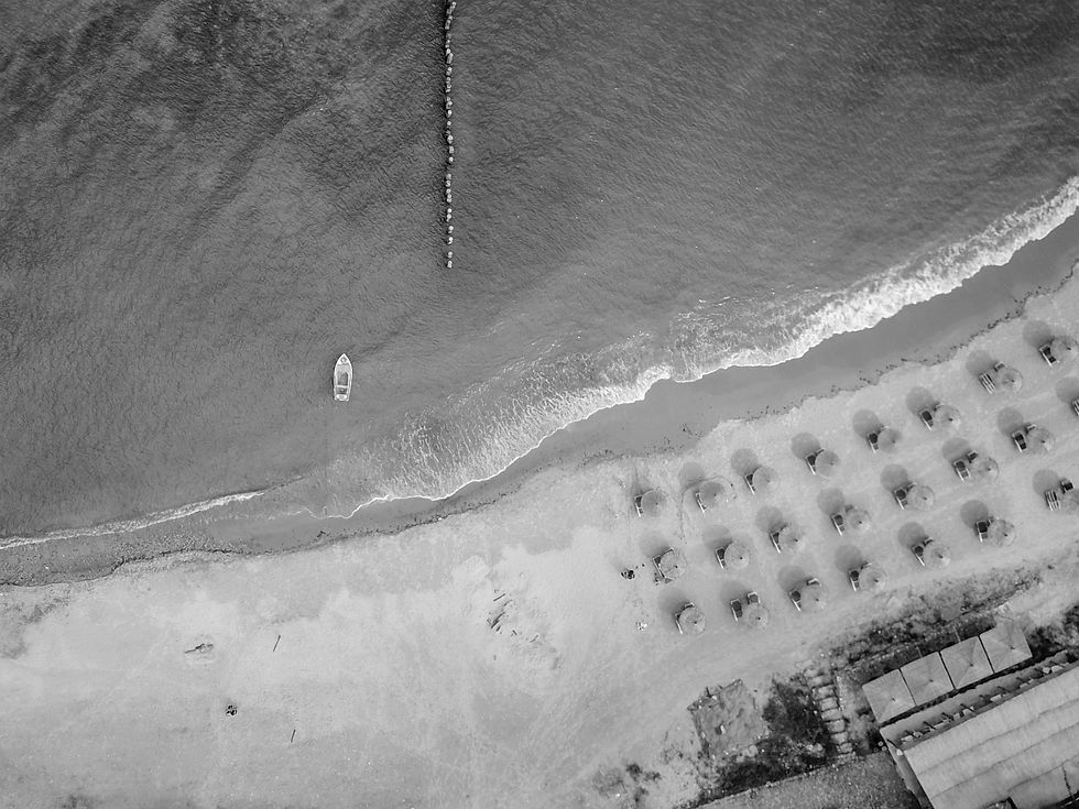 Aerial view of an Albanian beach with waves hitting the shore and a grid-like structure visible on the sand, captured by Wild Kind Photography.