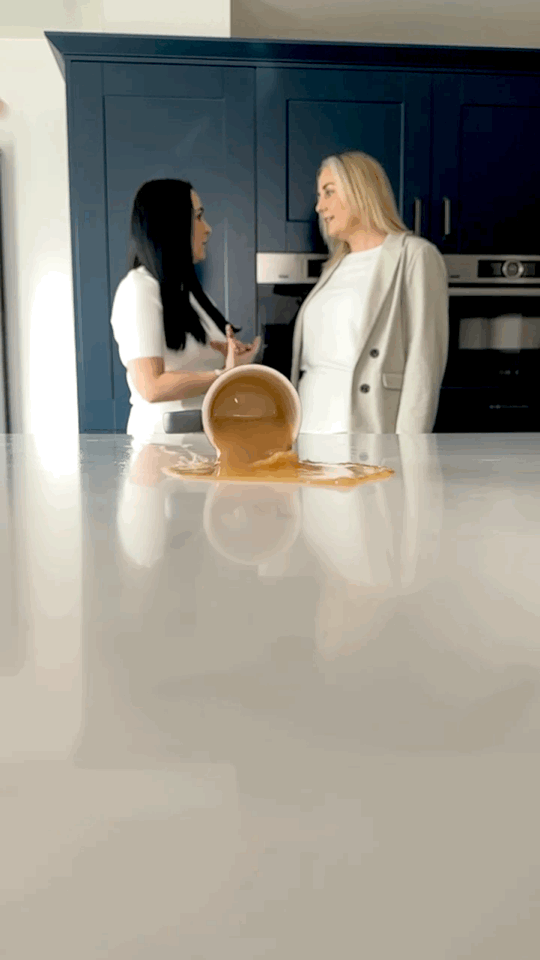GIF of tea spilling across countertop with two women speaking in background.