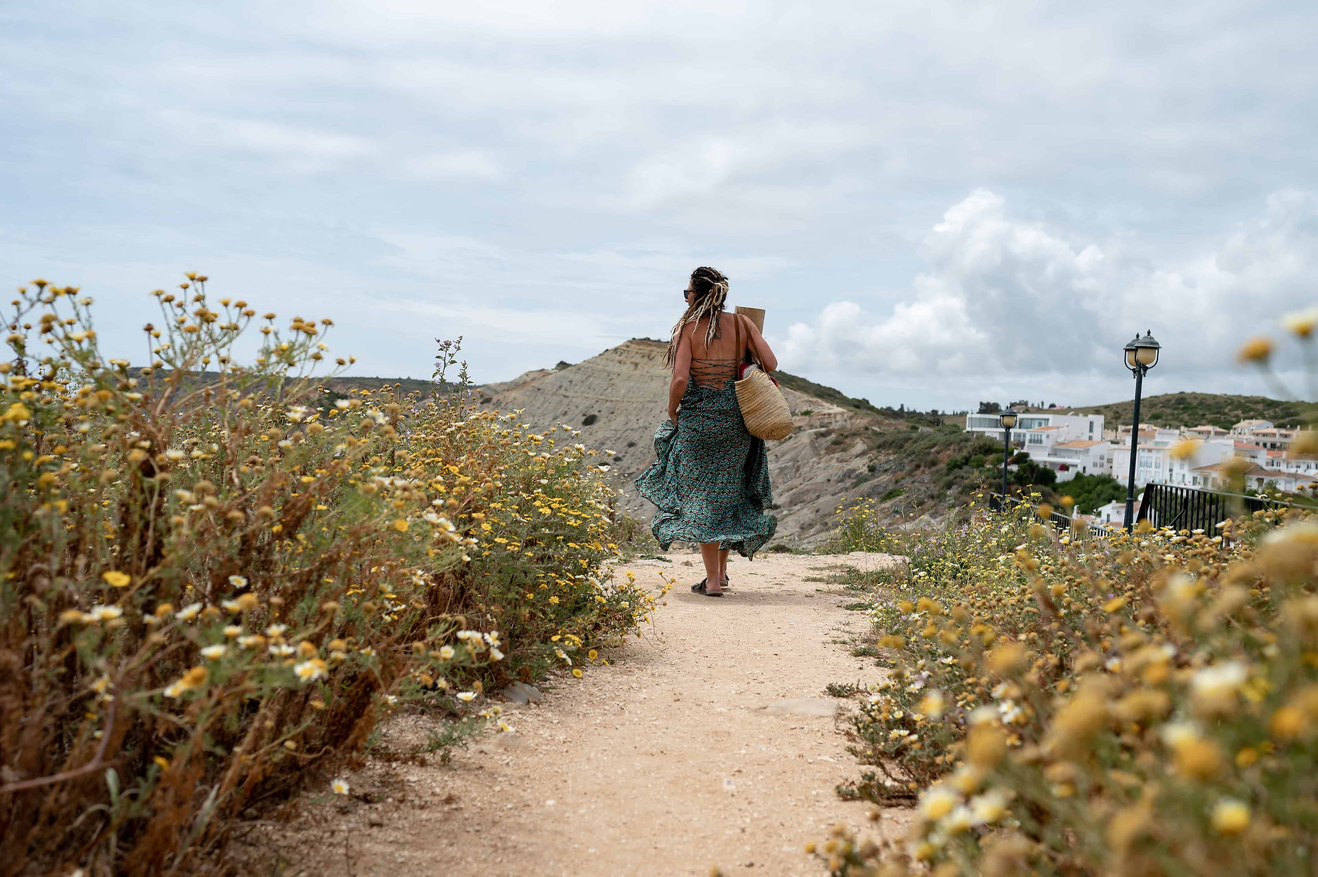 Yoga instructor Chloe Ward walking along wildflower path holding yoga mat on the cliffs above Burgau, Portugal.