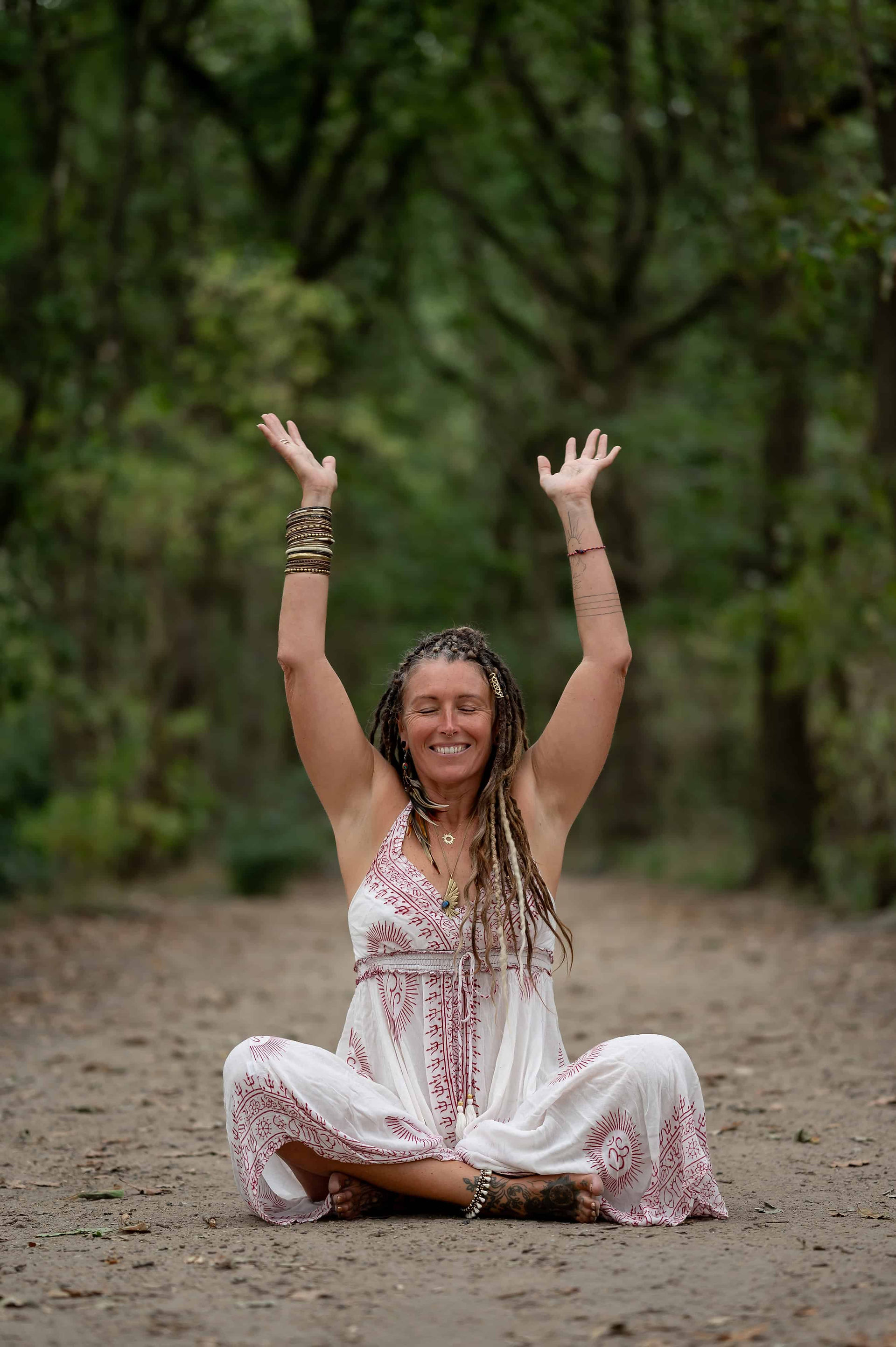 Wellness instructor sitting cross-legged in forest with arms lifted in a grounding pose during Wirral Brand Shoot.