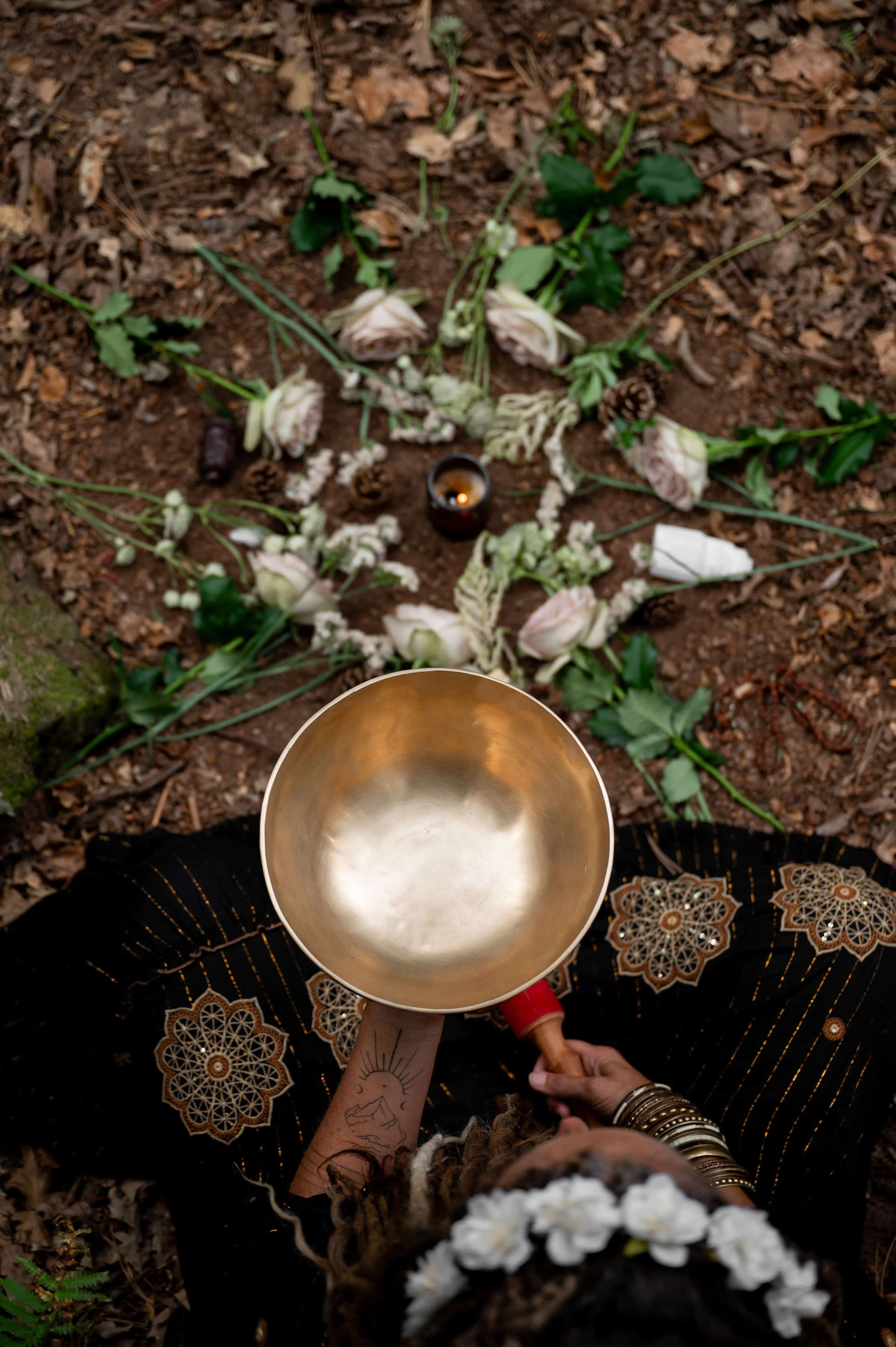 Singing bowl held above floral ritual circle on forest floor.