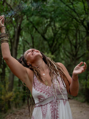Woman dancing freely in forest with arms raised in joy.