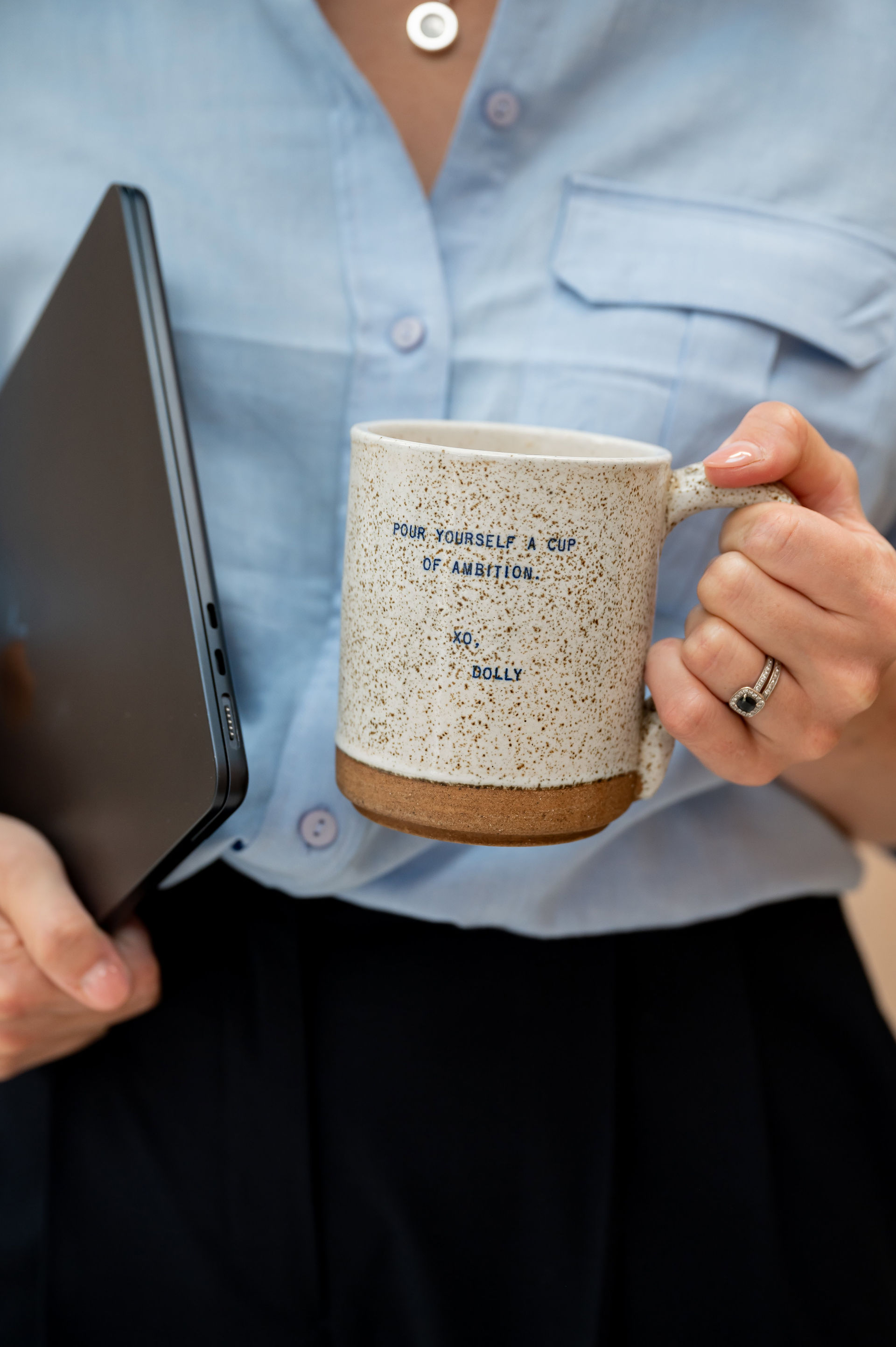 During her brand shoot for Surviving in Scrubs, Dr. Chelcie Jewitt holds a laptop and a speckled mug reading "Pour yourself a cup of ambition."
