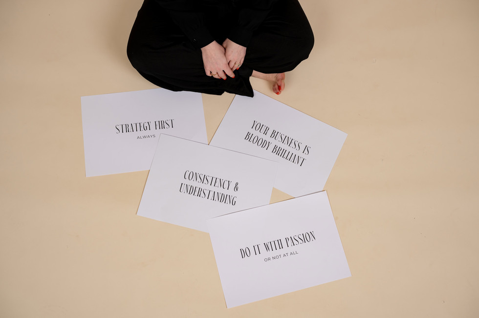 Brand designer sitting on floor with signs that read “Strategy First,” “Connection & Understanding,” and “Do it With Passion.”