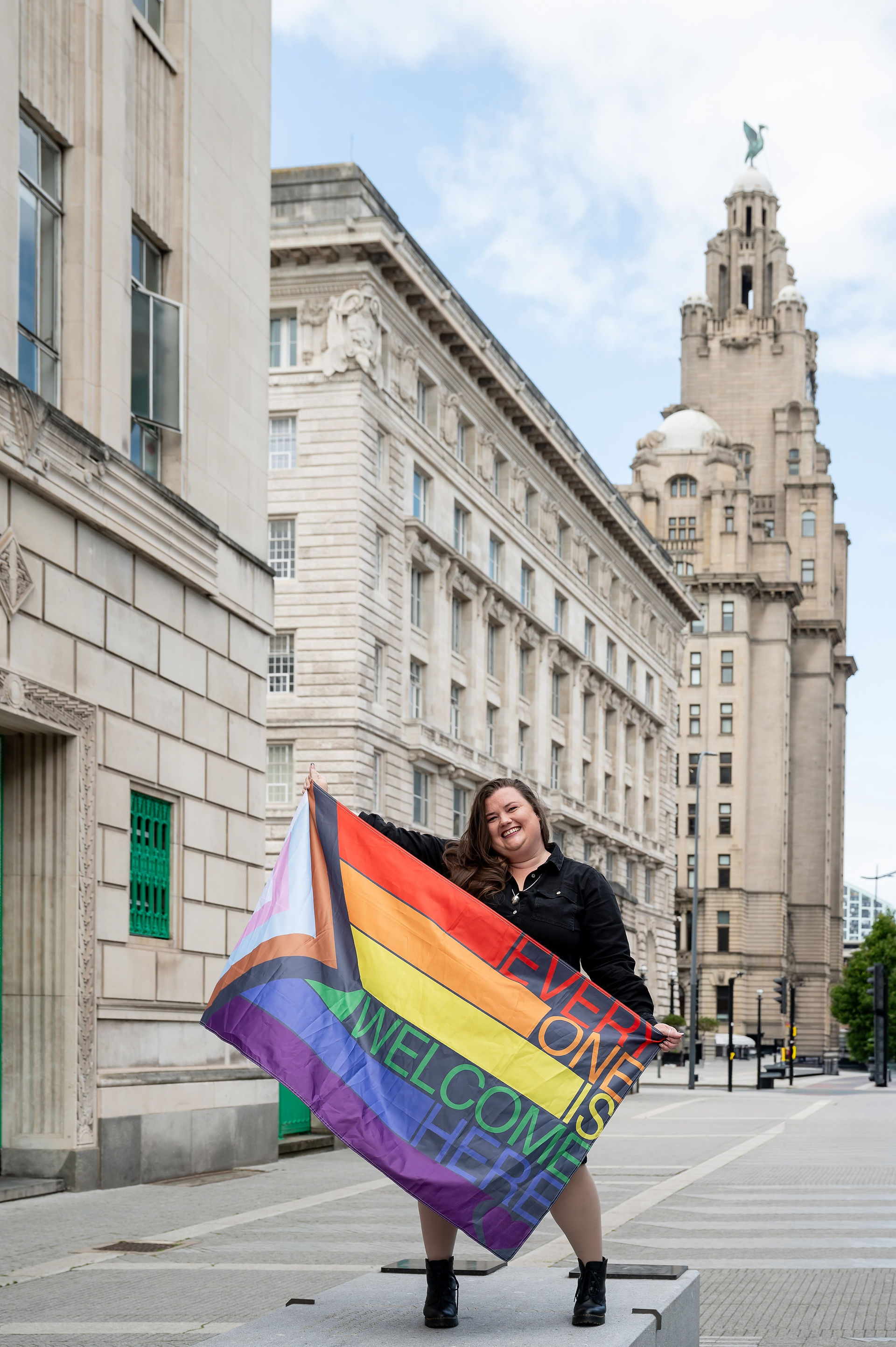 Woman standing in front of Liver building holding a pride flag in Liverpool.