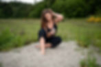 Brand shoot of a barefoot woman in black sitting on the sand, holding tarot cards in a field of greenery in Seattle, WA.