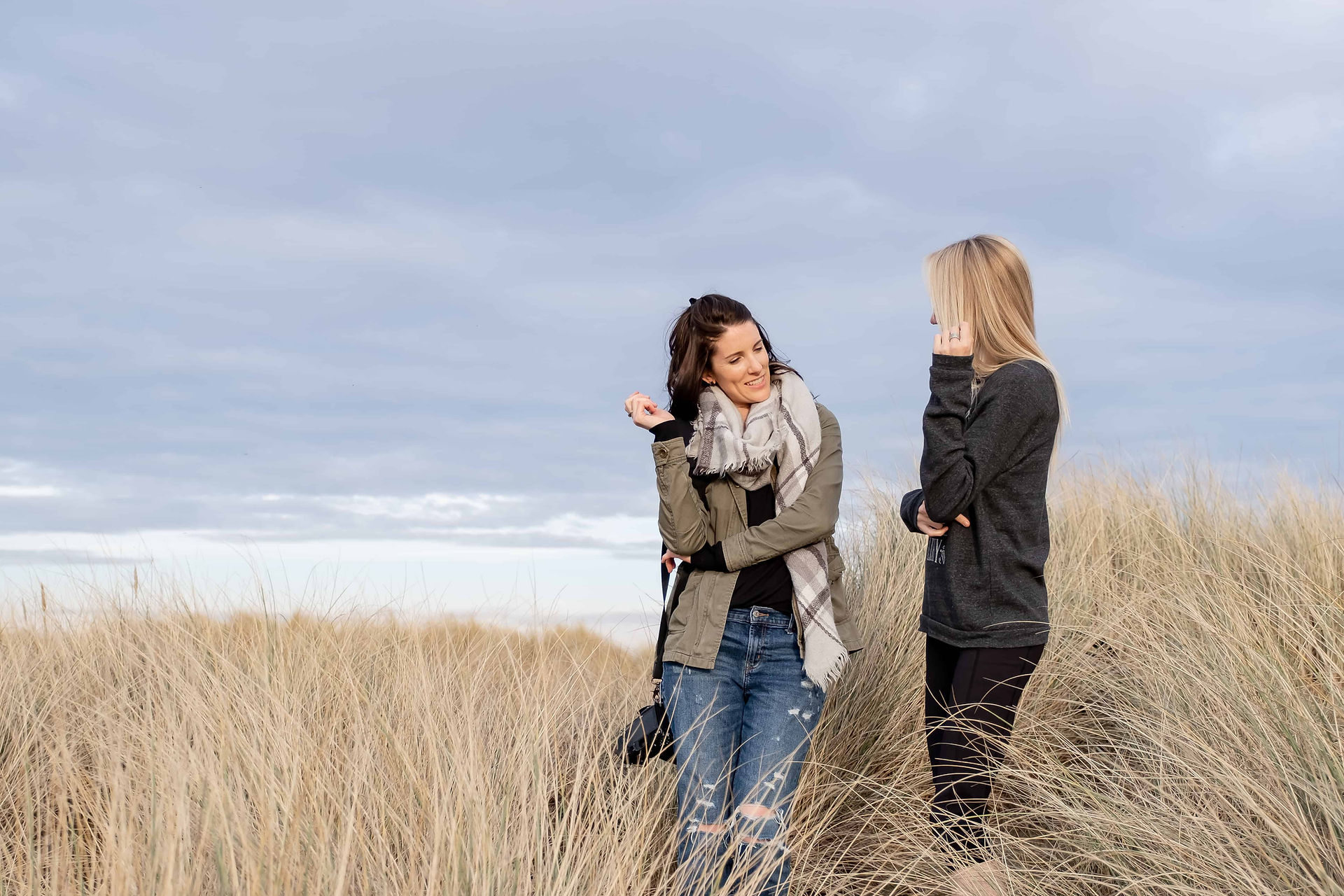 Behind-the-scenes moment of photographer showing client how to pose during a brand photoshoot at the English coast, among the sand dunes.