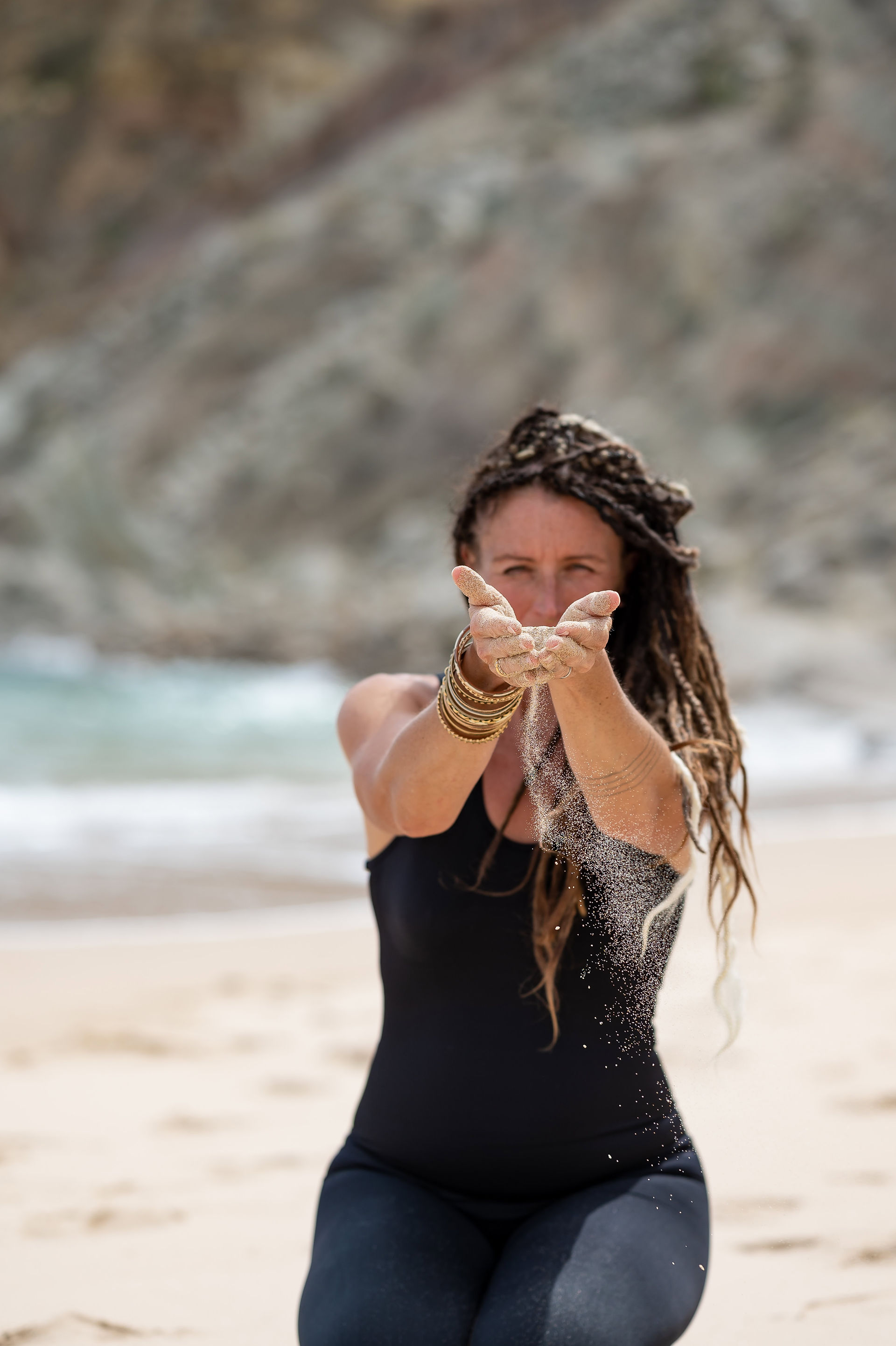 Yoga instructor Chloe Ward letting sand slip through hands on beach in the Algarve, Portugal during personal branding photoshoot abroad with Wild Kind Photography.