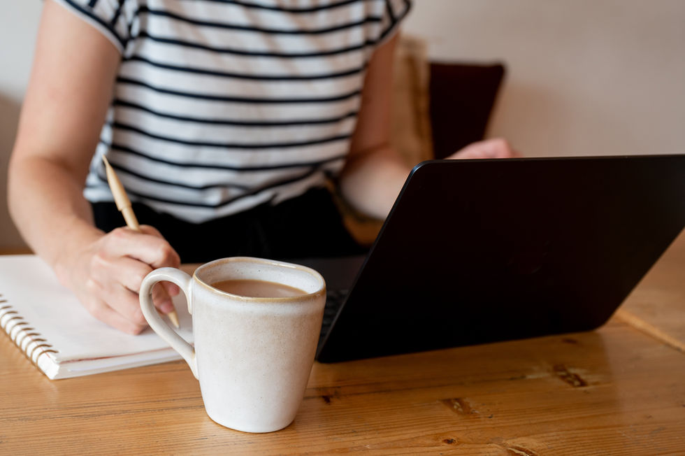 Seated at a cafe table, during a brand shoot, Dr. Chelcie Jewitt from Surviving in Scrubs jots notes in a notebook while navigating her laptop.