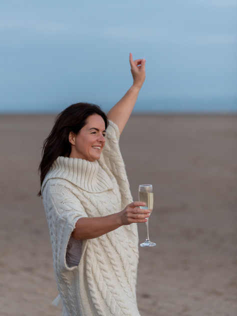 Functional medicine expert on a Wirral beach, holding a champagne glass and smiling.