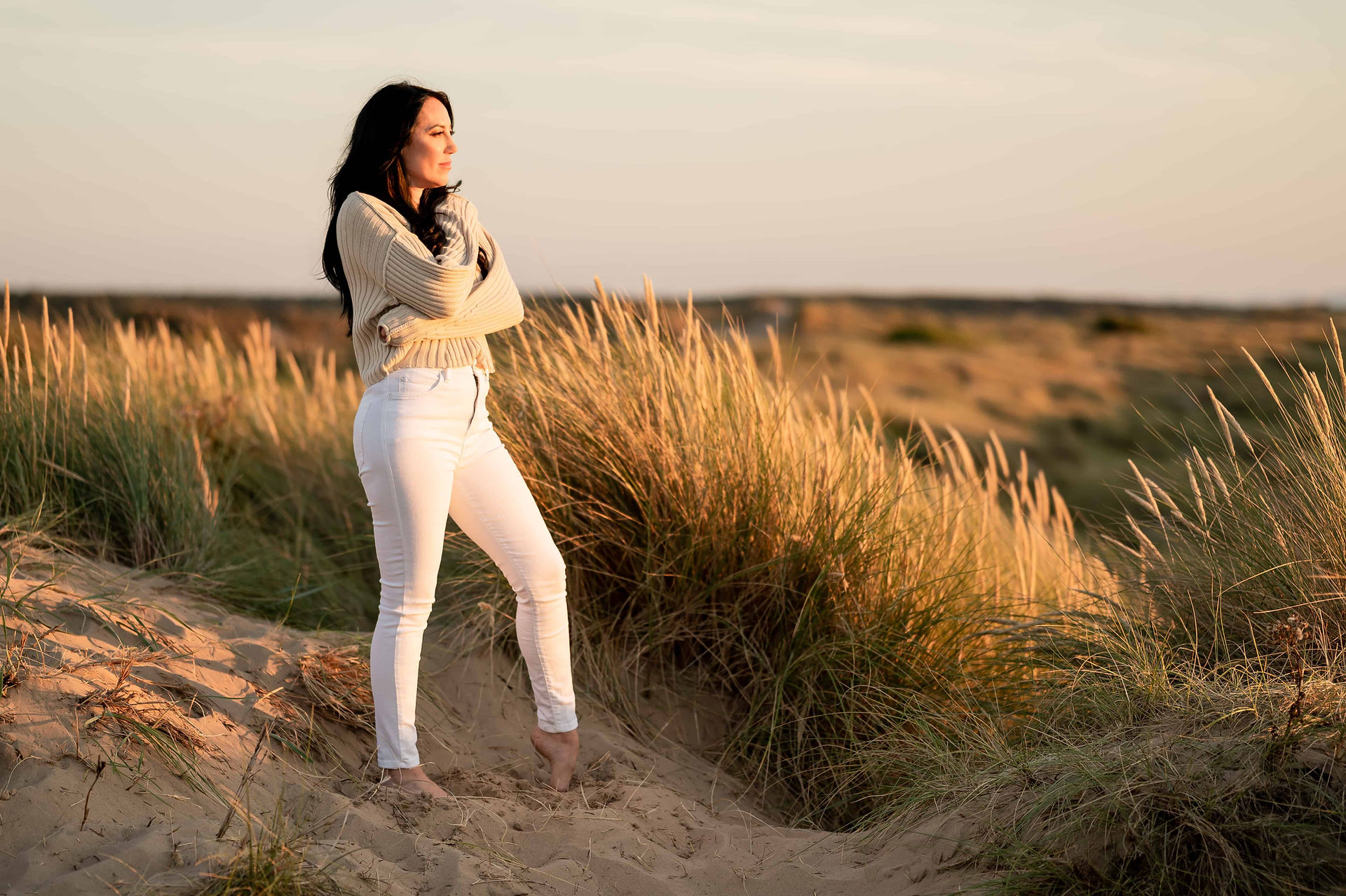 Hypnotherapist hugging herself in dunes at Ainsdale Beach.